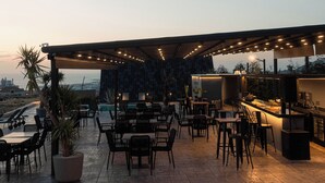 Een buitenterras met tafels, stoelen, een bar en een uitzicht op de stad.