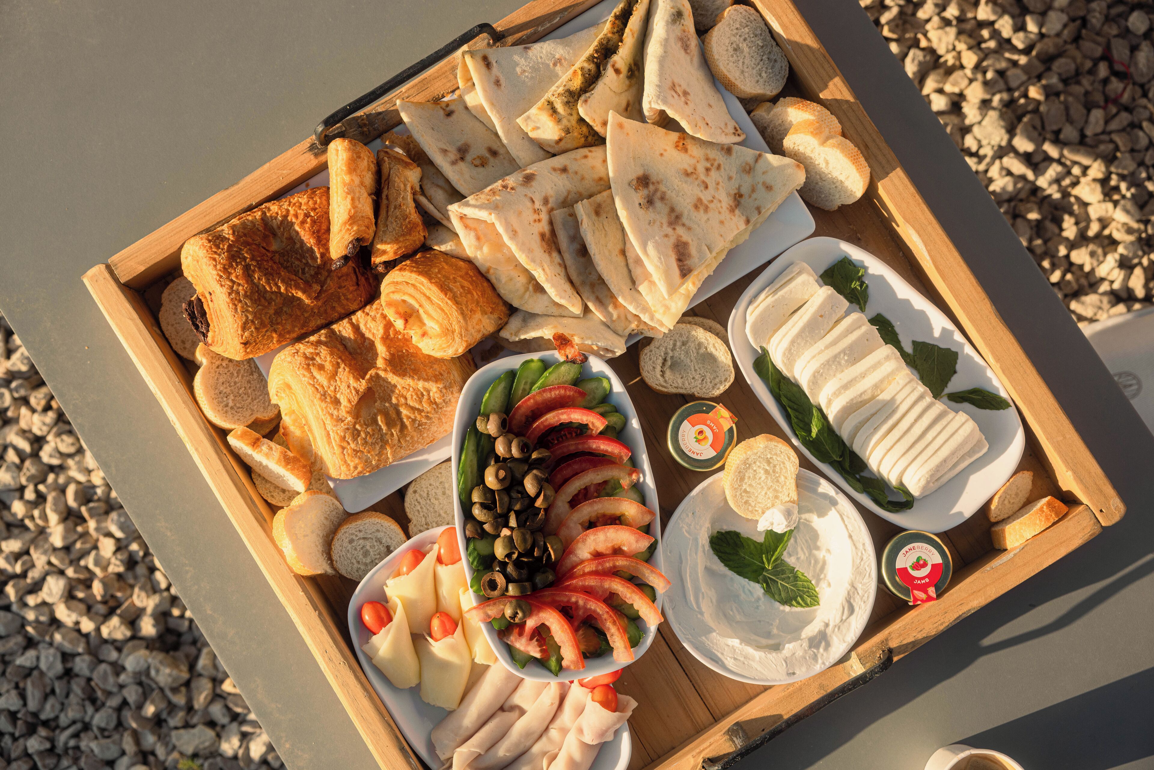 Ein Holztablett mit verschiedenen Speisen, darunter Brot, Käse, Tomaten, Oliven und einer Scheibe Brot.