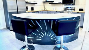 A modern kitchen with a central island, stainless steel appliances, and black bar stools. - Modern Studio Home SolMod # 1 (Tucson)