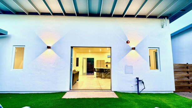 A modern house with a covered patio, a well-maintained lawn, and a visible kitchen area. - Modern Studio Home SolMod # 1 (Tucson)