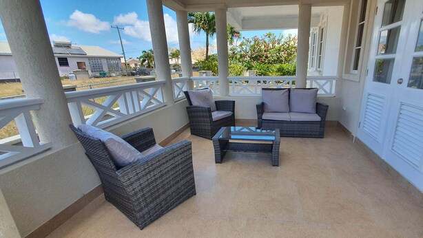 A covered balcony with wicker furniture and a glass table, overlooking a residential area. - Infinity Townhomes, Charming 3-bedroom, 3.5 bathroom townhouse, AC, fitness room (Bagatelle Terrace)