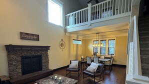 A spacious living room with a stone fireplace, a dining area with a high ceiling and a balcony, and a cozy atmosphere. - Flagstaff Family Retreat — Game Room, Gym, Fire Pit & Forest Fun! (Flagstaff)