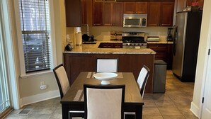 A modern kitchen with wooden cabinets, a stainless steel refrigerator, and a dining area with a table and chairs. - Flagstaff Family Retreat — Game Room, Gym, Fire Pit & Forest Fun! (Flagstaff)