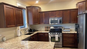 A kitchen with dark wood cabinets, a stainless steel stove, a microwave, and a refrigerator. - Flagstaff Family Retreat — Game Room, Gym, Fire Pit & Forest Fun! (Flagstaff)