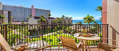 Varanda com móveis de vime, uma mesa pequena com uma bebida e vista para um hotel e praia.