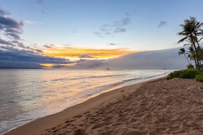 A beach with a clear sky, calm sea, and a sunset.