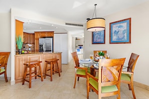 Una cocina moderna con armarios de madera, una isla central con taburetes y un comedor con mesa de vidrio y sillas.