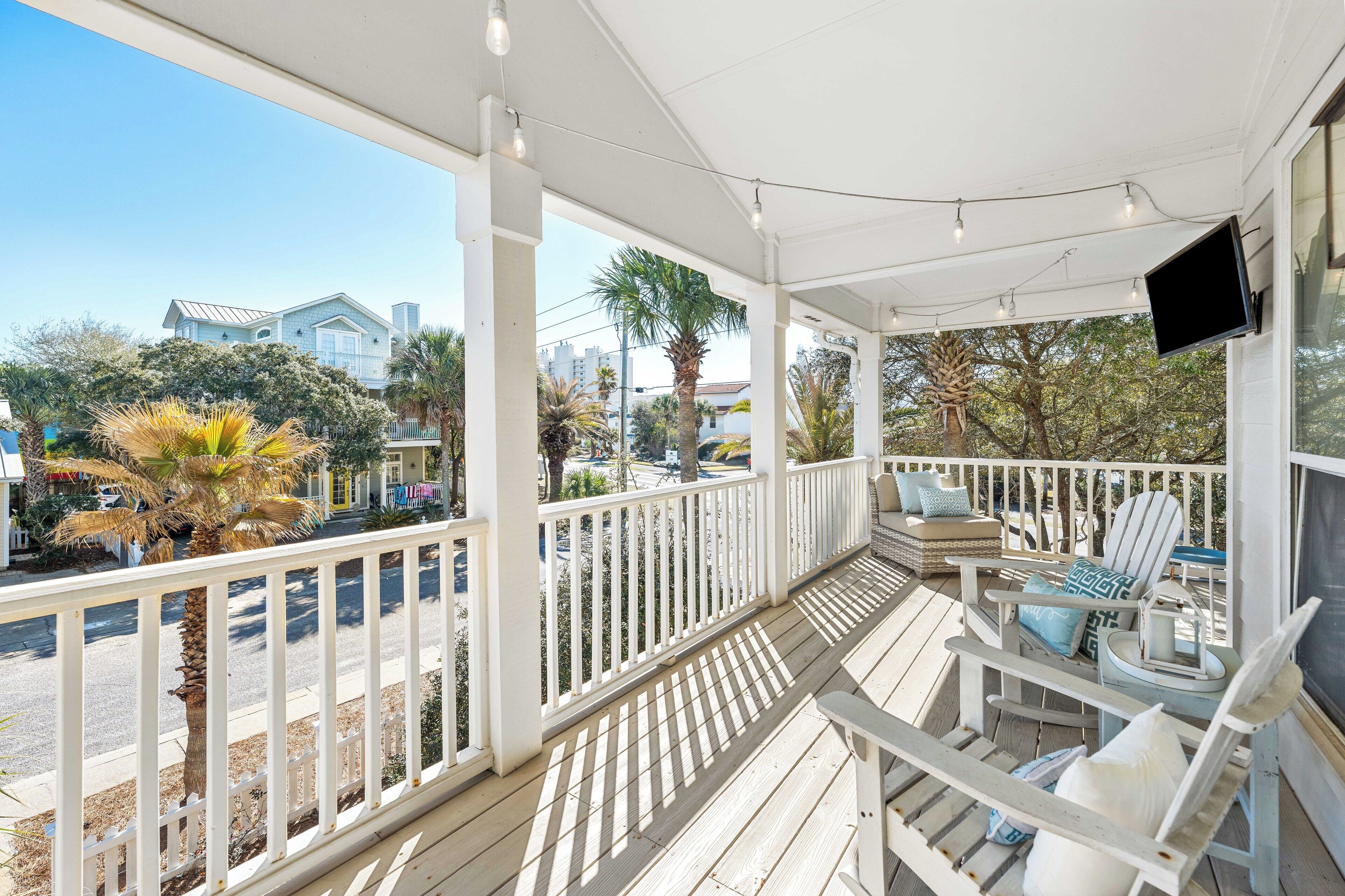 A covered porch with white railings, a flat-screen TV mounted on the wall, and outdoor furniture including chairs and a table.
