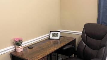 Un bureau d’angle avec un bureau en bois, un fauteuil en cuir noir, une petite plante en pot et une horloge numérique.