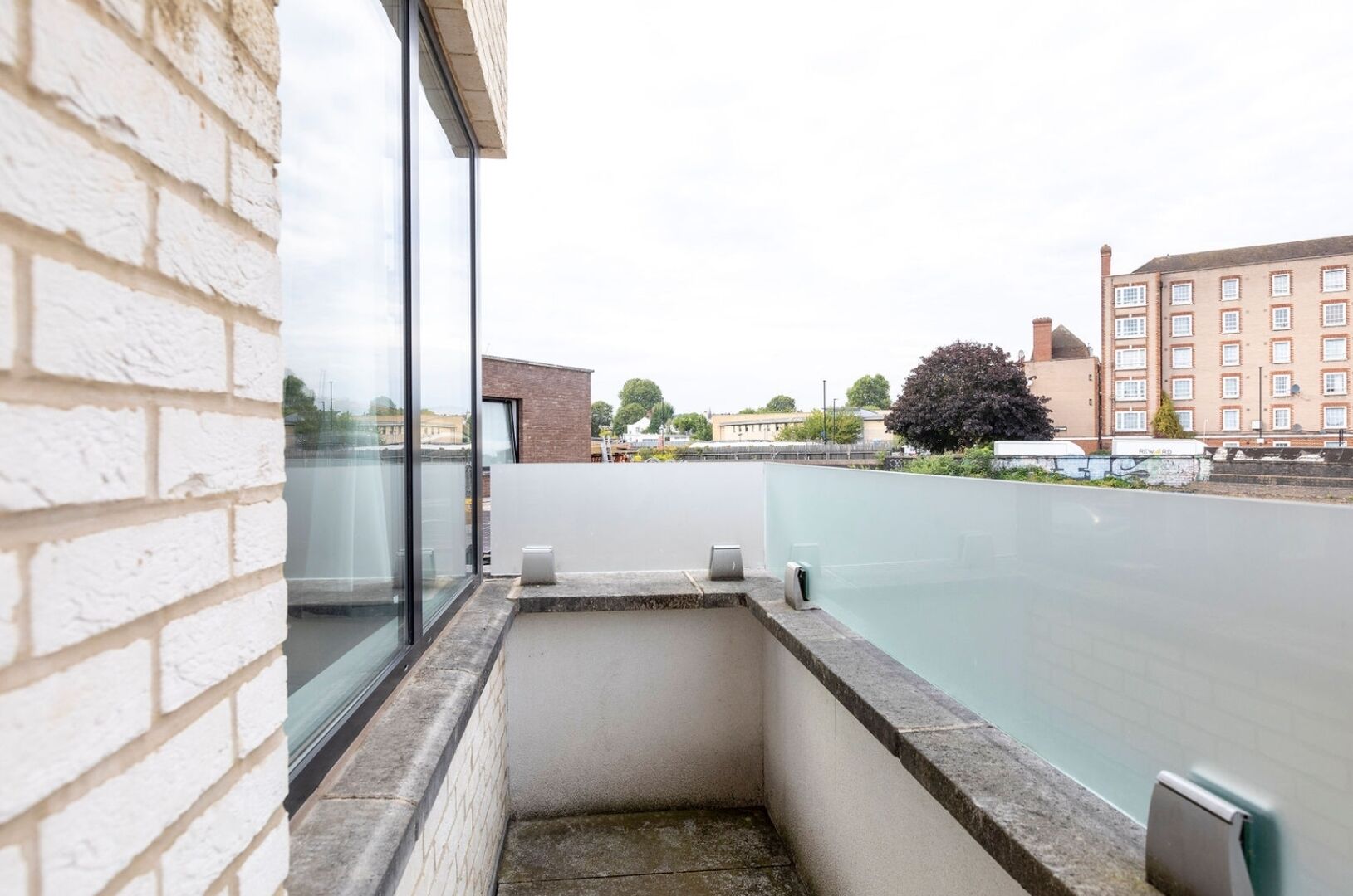 Ein schmaler Balkon mit Glaswand, einem kleinen Podest und einem Metallgeländer.