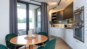 A modern kitchen with white cabinets, stainless steel appliances, and a dining area with a round table and green chairs. - Modern Flat with Private Balcony | Lift access (Greater London)