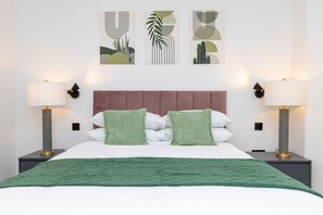 A neatly arranged hotel room with a large bed, two bedside lamps, and three wall art pieces. - Modern Flat with Private Balcony | Lift access (Greater London)