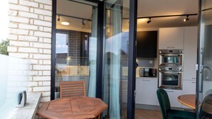 A modern kitchen with built-in appliances, a dining area with a wooden table and chairs, and a glass door leading to an outdoor space. - Modern Flat with Private Balcony | Lift access (Greater London)