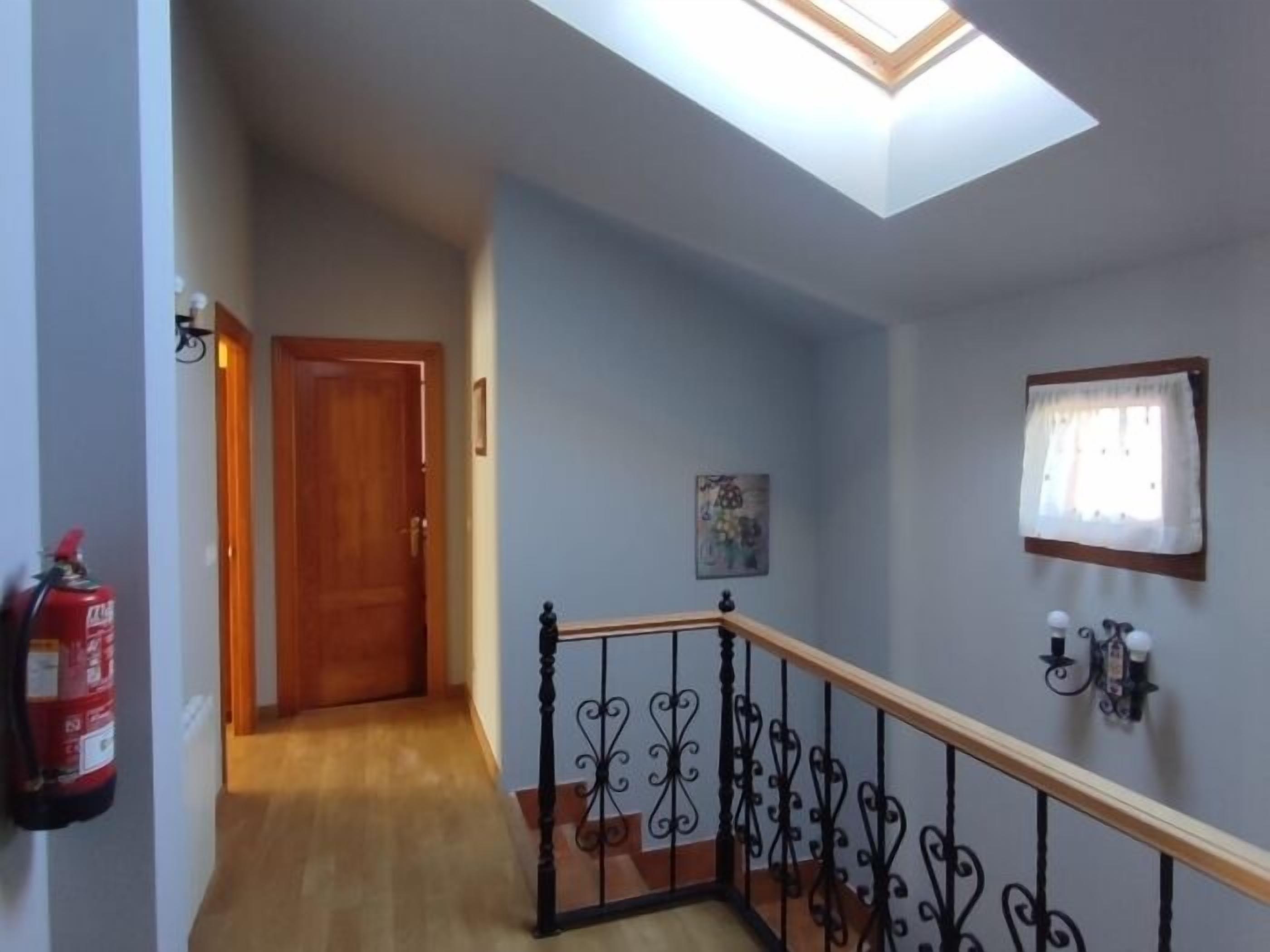A hallway with a wooden door, a fire extinguisher, a skylight, and a staircase with a wrought iron railing.