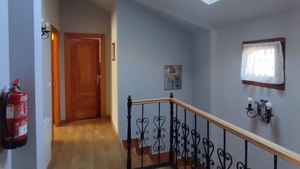 Un pasillo con una puerta de madera, un extintor, un tragaluz y una escalera con barandilla de hierro forjado.