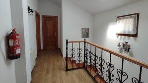 Un pasillo con suelo de madera, barandilla de metal negro, extintor, puerta de madera y tragaluz.