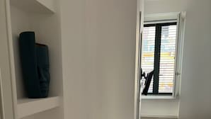 Un couloir étroit mène à une chambre à coucher qui contient un lit et une fenêtre avec des stores.