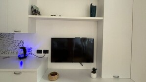 Une cuisine moderne avec des meubles blancs, un téléviseur à écran plat fixé au mur et un appareil de climatisation installé au-dessus.