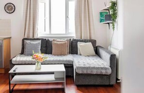 A modern living room with a grey sectional sofa, a white coffee table, and a vase with flowers. - Beautiful view Apt
Near Canary Wharf (London)