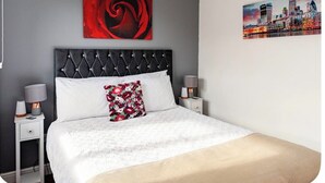 A bed with a tufted headboard, two bedside tables with lamps, a floral pillow, and two wall art pieces. - Beautiful view Apt
Near Canary Wharf (London)
