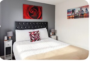 A bed with a tufted headboard, two bedside tables with lamps, a floral pillow, and two wall art pieces.