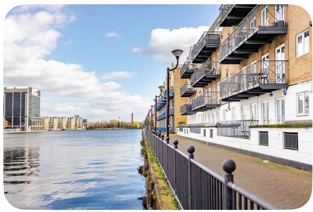 Un paseo fluvial con edificios modernos, cielo despejado y una masa de agua tranquila.