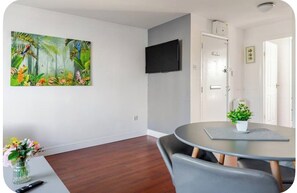 Une pièce avec une table ronde, un téléviseur à écran plat fixé au mur et une porte donnant sur une autre pièce.
