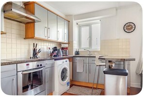 Une cuisine compacte équipée d’un four encastré, d’un lave-linge et d’un évier.