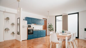 Une cuisine moderne avec des meubles bleus, un réfrigérateur blanc et un coin repas comprenant une table et des chaises blanches.