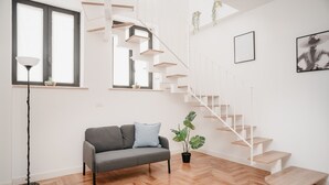 Un salon moderne avec un canapé gris, un lampadaire noir, un escalier avec des rampes blanches et une plante en pot.