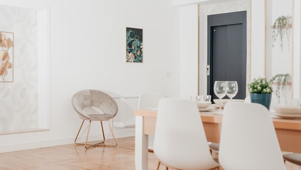 Un espace repas moderne avec une table en bois, des chaises blanches et une œuvre d’art encadrée accrochée au mur.