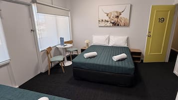 Habitación de hotel con dos camas, un escritorio, una silla, una pizarra y una puerta marcada con el número 19.