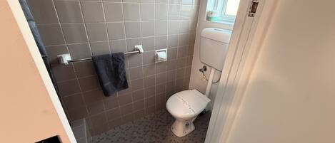 A bathroom with a toilet, a towel rack, and a window.