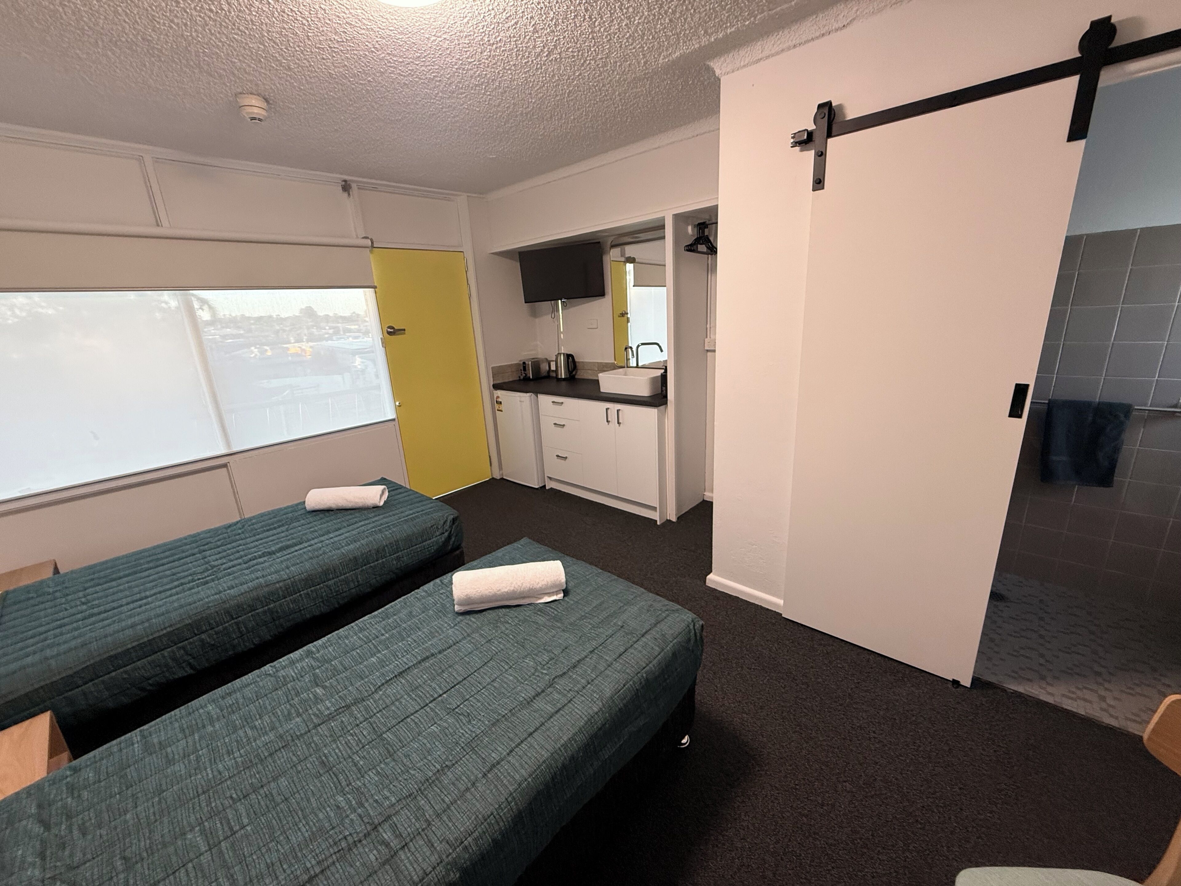 Quarto com duas camas, cozinha compacta, banheiro e porta deslizante.