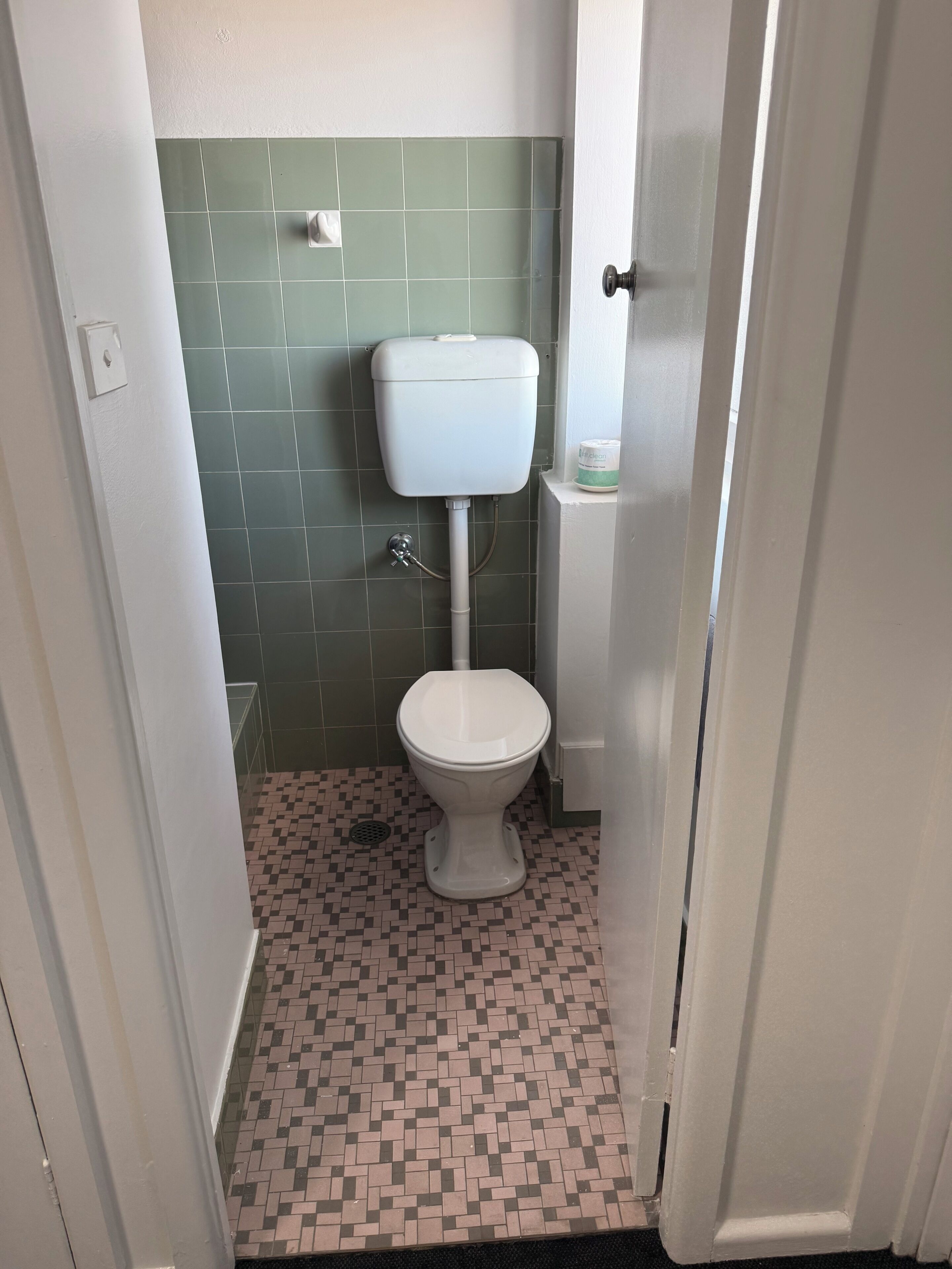 A small bathroom with a toilet, a tiled floor, and a green wall.