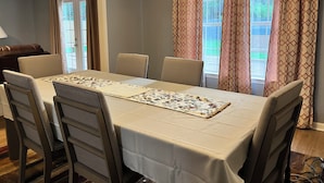 A dining area with a table set for six, surrounded by chairs, a chandelier, and patterned curtains. - Spacious 4-bedroom house in charming Memphis with AC, WiFi (Memphis)