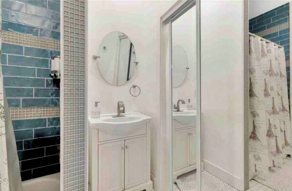 A bathroom with a white sink, two round mirrors, and a shower with a curtain featuring Eiffel Tower designs.