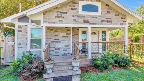 A two-story house with a stone facade, a front porch with a wooden railing, and a small front yard with potted plants. - Charming 2-bedroom house with AC and WiFi in cool Houston (Houston)