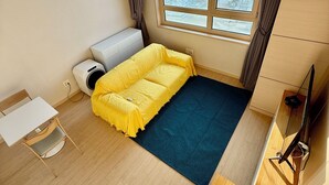 A compact room with a bed, a small table, a chair, a TV, and a window with a city view.