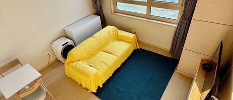 A compact room with a bed, a small table, a chair, a TV, and a window with a city view.