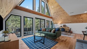 A spacious living area with a green sofa, a coffee table, and a view of a balcony with outdoor furniture. - The Chalet - A Frame in the Overlook, close to Saddleback! (Rangeley)