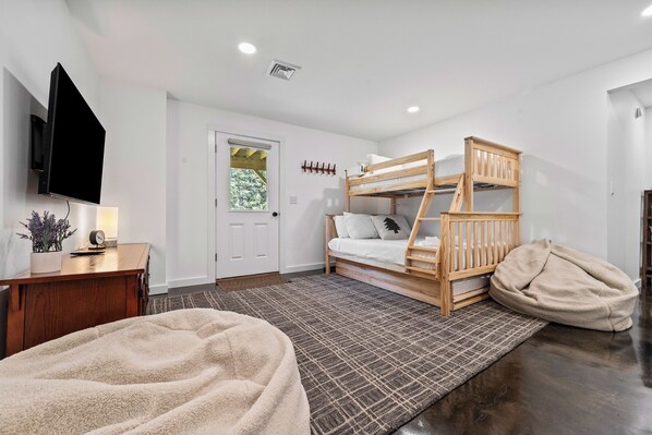 A bedroom with a bunk bed, a desk with a lamp, a TV mounted on the wall, and a door with a window. - The Chalet - A Frame in the Overlook, close to Saddleback! (Rangeley)