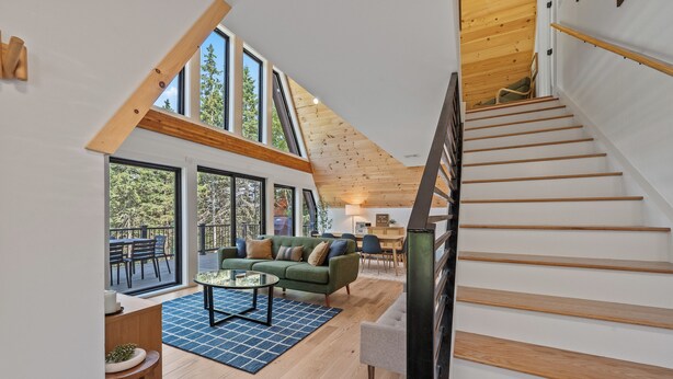 A modern interior with a staircase, wooden flooring, a green sofa, and large windows. - The Chalet - A Frame in the Overlook, close to Saddleback! (Rangeley)