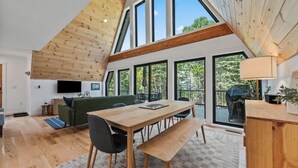 A modern interior with a wooden ceiling, large windows, a dining table, and a green sofa. - The Chalet - A Frame in the Overlook, close to Saddleback! (Rangeley)