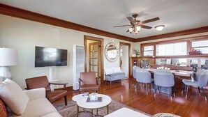 A spacious living room with a flat-screen TV, comfortable seating, a dining area with a table and chairs, and a ceiling fan.