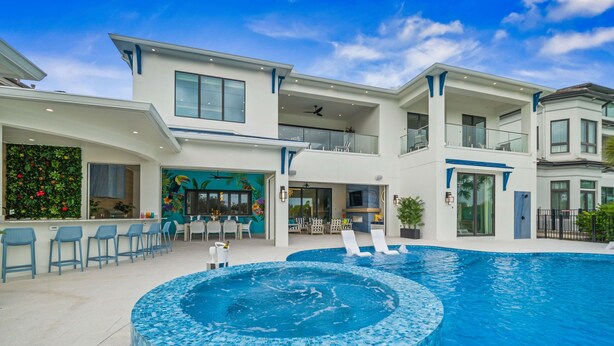 Une maison moderne à deux étages dotée d’une grande piscine, d’un espace salon extérieur et d’un patio.