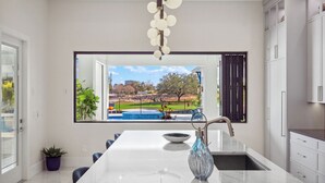 Une cuisine moderne dotée d’un grand îlot central, offrant une vue sur un parc, et comprenant un coin repas avec des chaises bleues.