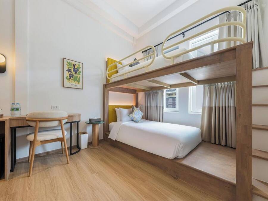 A bunk bed room with a desk, chair, and a small trash bin.