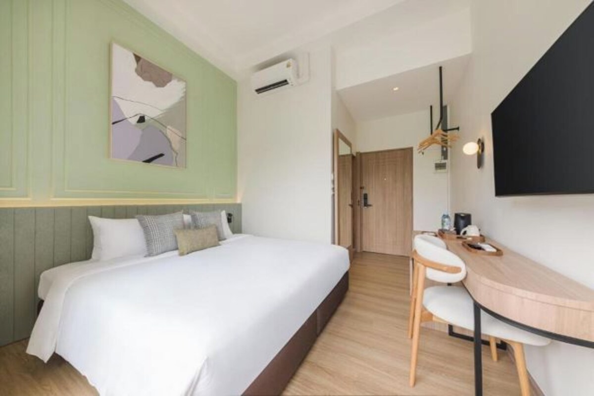 A hotel room with a bed, a desk, and a chair. There is a painting on the wall and a door leading to another room.