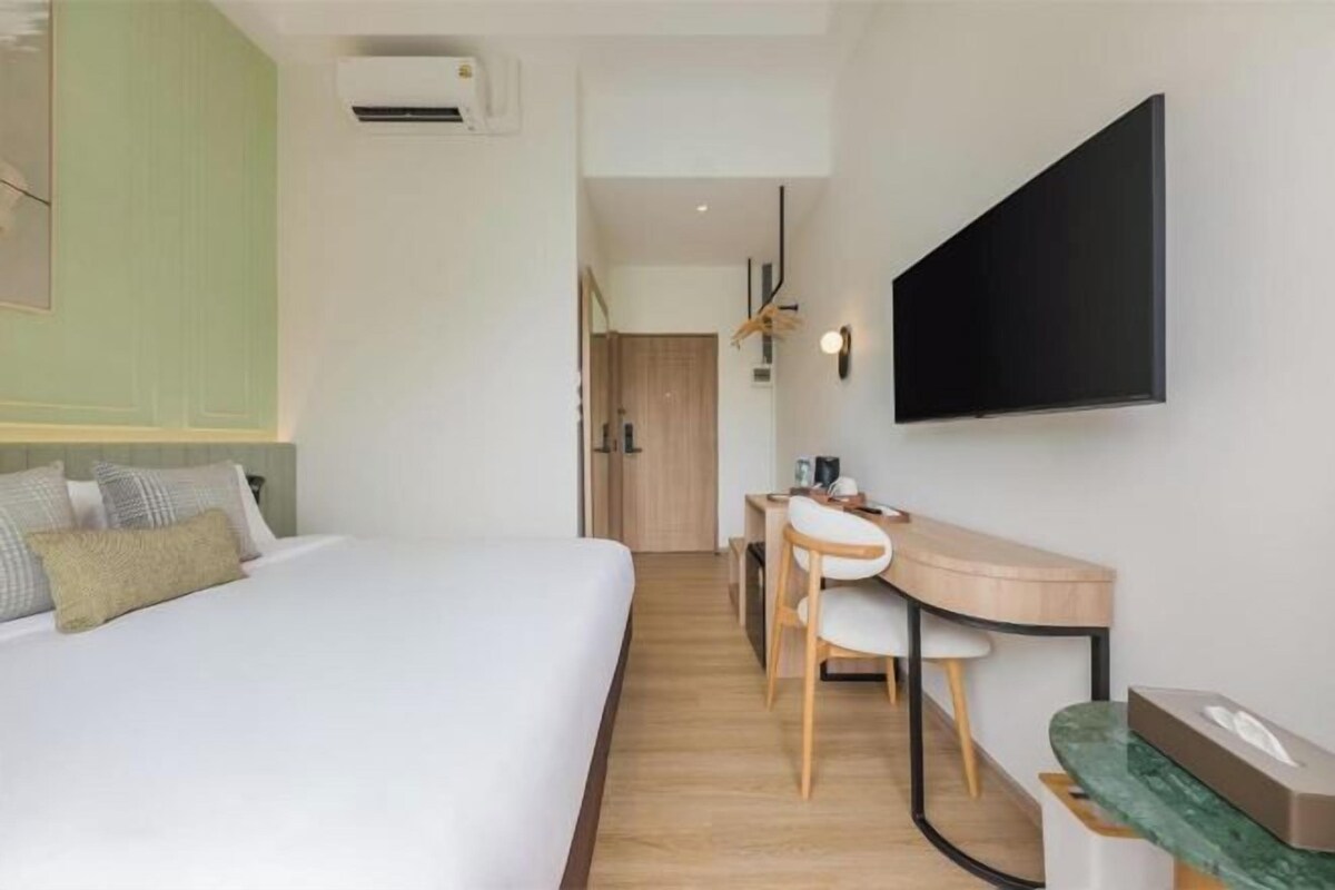 A hotel room with a bed, desk, chair, and a television mounted on the wall.